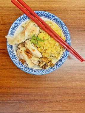 Resim, sıcak, yatay tahıllı ahşap bir masa üzerine kurulmuş mavi ve beyaz bir seramik kasede servis edilen erişte kâsesini yukarıdan aşağıya doğru gösteriyor..