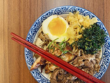 Mavi ve beyaz desenli seramik bir kasede servis edilen canlı bir Japon pirinç kasesinin yukarıdan aşağı görüntüsü. Bir çift parlak kırmızı çubuk üst tarafta köşegen olarak duruyor..