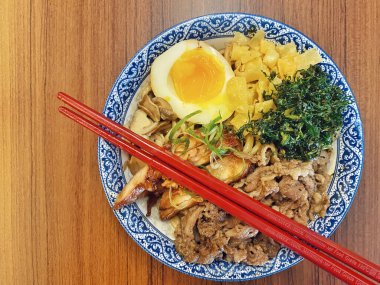 Mavi ve beyaz desenli seramik bir kasede servis edilen canlı bir Japon pirinç kasesinin yukarıdan aşağı görüntüsü. Bir çift parlak kırmızı çubuk üst tarafta köşegen olarak duruyor..