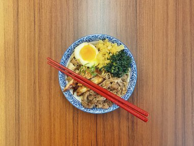 Mavi ve beyaz desenli seramik bir kasede servis edilen canlı bir Japon pirinç kasesinin yukarıdan aşağı görüntüsü. Bir çift parlak kırmızı çubuk üst tarafta köşegen olarak duruyor..