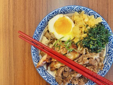 Mavi ve beyaz desenli seramik bir kasede servis edilen canlı bir Japon pirinç kasesinin yukarıdan aşağı görüntüsü. Bir çift parlak kırmızı çubuk üst tarafta köşegen olarak duruyor..