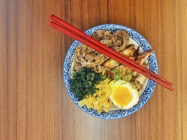 Mavi ve beyaz desenli seramik bir kasede servis edilen canlı bir Japon pirinç kasesinin yukarıdan aşağı görüntüsü. Bir çift parlak kırmızı çubuk üst tarafta köşegen olarak duruyor..