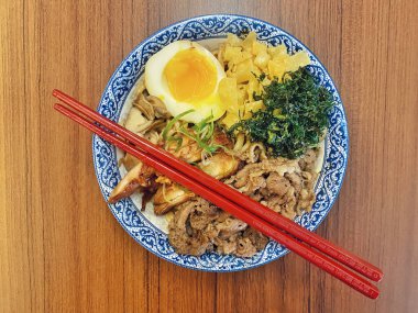 Mavi ve beyaz desenli seramik bir kasede servis edilen canlı bir Japon pirinç kasesinin yukarıdan aşağı görüntüsü. Bir çift parlak kırmızı çubuk üst tarafta köşegen olarak duruyor..