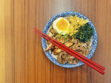 Mavi ve beyaz desenli seramik bir kasede servis edilen canlı bir Japon pirinç kasesinin yukarıdan aşağı görüntüsü. Bir çift parlak kırmızı çubuk üst tarafta köşegen olarak duruyor..