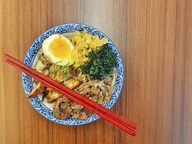 Mavi ve beyaz desenli seramik bir kasede servis edilen canlı bir Japon pirinç kasesinin yukarıdan aşağı görüntüsü. Bir çift parlak kırmızı çubuk üst tarafta köşegen olarak duruyor..