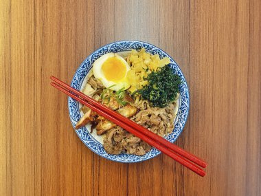 Mavi ve beyaz desenli seramik bir kasede servis edilen canlı bir Japon pirinç kasesinin yukarıdan aşağı görüntüsü. Bir çift parlak kırmızı çubuk üst tarafta köşegen olarak duruyor..