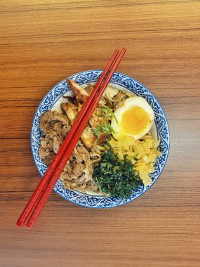 Mavi ve beyaz desenli seramik bir kasede servis edilen canlı bir Japon pirinç kasesinin yukarıdan aşağı görüntüsü. Bir çift parlak kırmızı çubuk üst tarafta köşegen olarak duruyor..