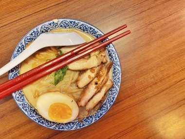 Ilık ahşap bir masanın üstünde duran mavi ve beyaz desenli seramik kasede titizlikle düzenlenmiş klasik bir ramen kasesinin canlı, tepeden tırnağa görüntüsü..