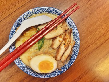 Ilık ahşap bir masanın üstünde duran mavi ve beyaz desenli seramik kasede titizlikle düzenlenmiş klasik bir ramen kasesinin canlı, tepeden tırnağa görüntüsü..