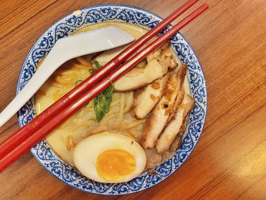 Ilık ahşap bir masanın üstünde duran mavi ve beyaz desenli seramik kasede titizlikle düzenlenmiş klasik bir ramen kasesinin canlı, tepeden tırnağa görüntüsü..