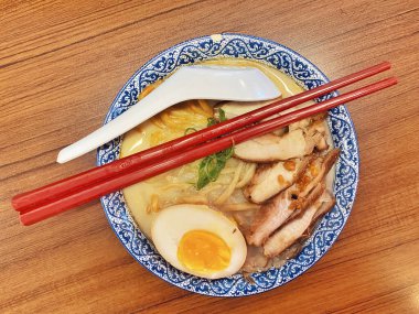 Ilık ahşap bir masanın üstünde duran mavi ve beyaz desenli seramik kasede titizlikle düzenlenmiş klasik bir ramen kasesinin canlı, tepeden tırnağa görüntüsü..