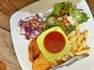 Canlı ve dengeli bir yemek, beyaz kare bir tabakta servis edilir, ince mavi kenarlı, kırsal bir ahşap masada dinlenir. Tavuk şnitzeli ya da balık ve patates kızartması tabağına benziyor. İki altın-kahverengi fileto ile karakterize edilmiş..