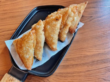 Bir tabak mükemmel altın, çıtır Samosas (veya kızartılmış wonton / empanada), modern siyah dikdörtgen tabakta servis edilir, ahşap saplı. Üçgenlerin kabuğunda çok güzel kabarcıklı bir doku var..