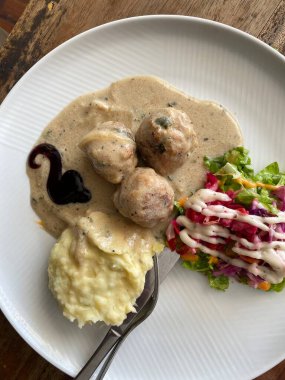 Beyaz desenli tabakta servis edilen İsveç usulü köfteler. Üç büyük, baharatlı köfte yumuşak, açık kahverengimsi bir sosta bol bol boğulur..