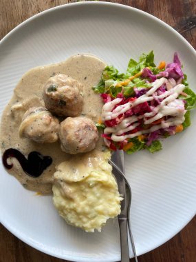 Beyaz desenli tabakta servis edilen İsveç usulü köfteler. Üç büyük, baharatlı köfte yumuşak, açık kahverengimsi bir sosta bol bol boğulur..