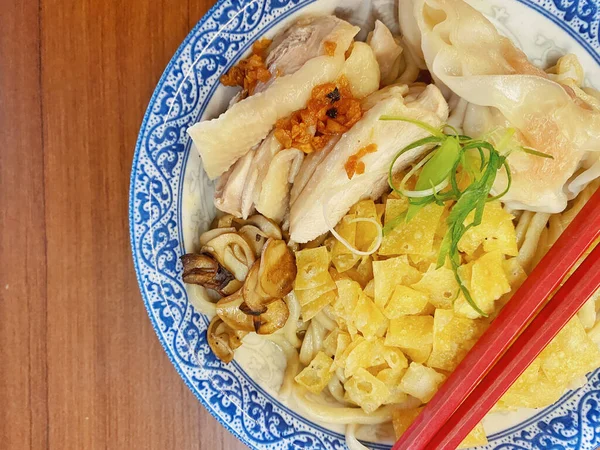 Resim, sıcak, yatay tahıllı ahşap bir masa üzerine kurulmuş mavi ve beyaz bir seramik kasede servis edilen erişte kâsesini yukarıdan aşağıya doğru gösteriyor..