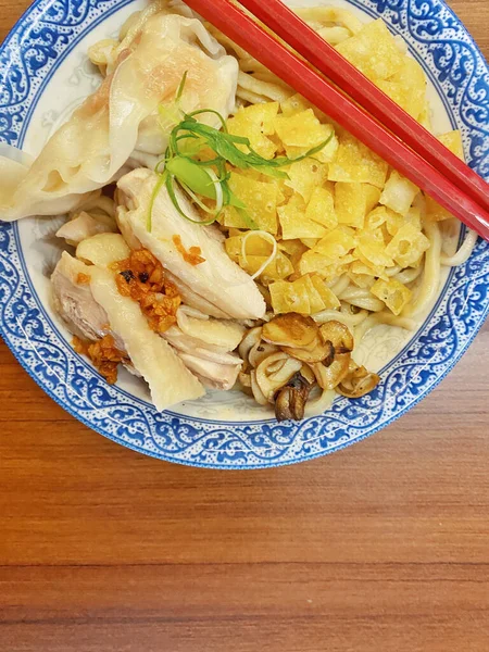 Resim, sıcak, yatay tahıllı ahşap bir masa üzerine kurulmuş mavi ve beyaz bir seramik kasede servis edilen erişte kâsesini yukarıdan aşağıya doğru gösteriyor..