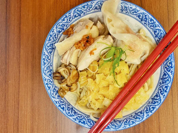 Resim, sıcak, yatay tahıllı ahşap bir masa üzerine kurulmuş mavi ve beyaz bir seramik kasede servis edilen erişte kâsesini yukarıdan aşağıya doğru gösteriyor..