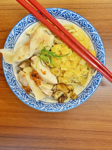 Resim, sıcak, yatay tahıllı ahşap bir masa üzerine kurulmuş mavi ve beyaz bir seramik kasede servis edilen erişte kâsesini yukarıdan aşağıya doğru gösteriyor..