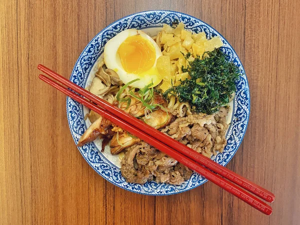 Mavi ve beyaz desenli seramik bir kasede servis edilen canlı bir Japon pirinç kasesinin yukarıdan aşağı görüntüsü. Bir çift parlak kırmızı çubuk üst tarafta köşegen olarak duruyor..