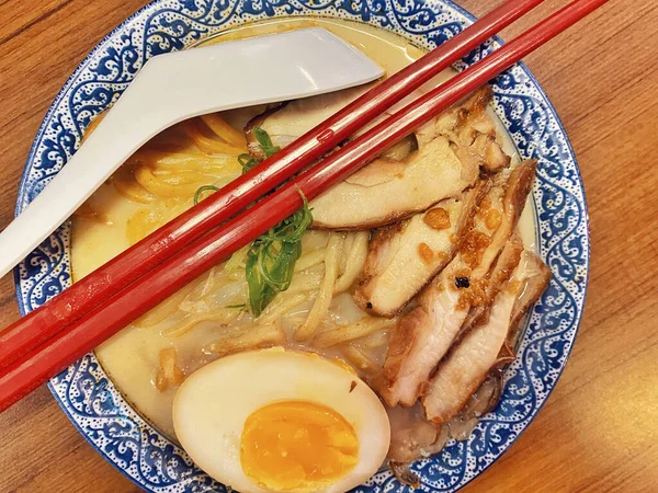 Ilık ahşap bir masanın üstünde duran mavi ve beyaz desenli seramik kasede titizlikle düzenlenmiş klasik bir ramen kasesinin canlı, tepeden tırnağa görüntüsü..