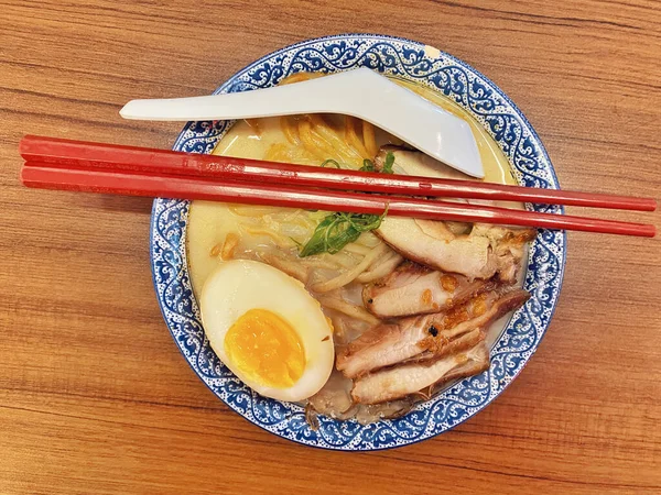 Ilık ahşap bir masanın üstünde duran mavi ve beyaz desenli seramik kasede titizlikle düzenlenmiş klasik bir ramen kasesinin canlı, tepeden tırnağa görüntüsü..