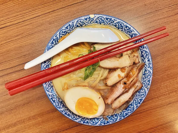 Ilık ahşap bir masanın üstünde duran mavi ve beyaz desenli seramik kasede titizlikle düzenlenmiş klasik bir ramen kasesinin canlı, tepeden tırnağa görüntüsü..