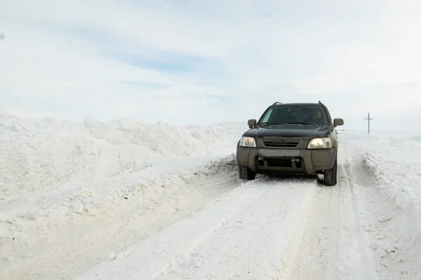 Male driver in a black dirty car on a winter road cleared of snow, drifts along the road. The concept of safe road traffic in winter