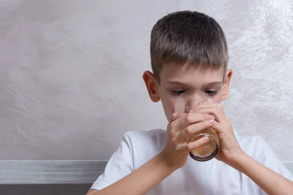 Un chico guapo bebe agua con gas de un vaso de vidrio, cerca, espacio para copiar. Concepto de alimentos poco saludables — Foto de Stock