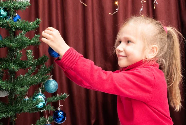 Cute Caucasian Cheerful Girl Red Sweater Hangs Festive Ball Decorated — Stock Photo, Image