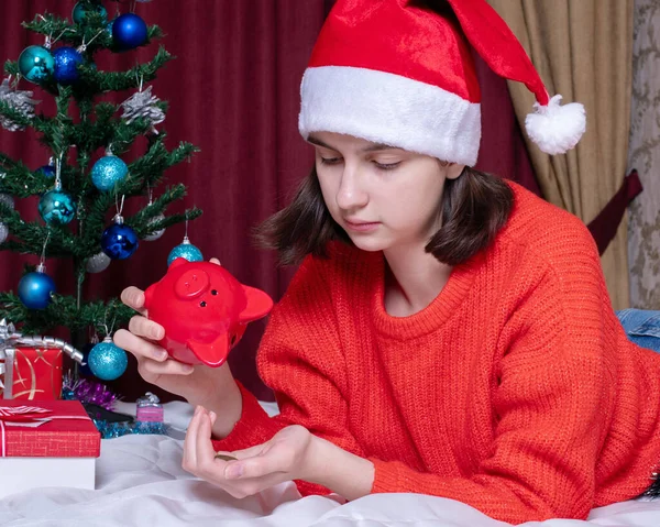 Smutna Dziewczyna Czerwonym Świątecznym Kapeluszu Swetrze Wylewa Monety Świnki Domowym — Zdjęcie stockowe