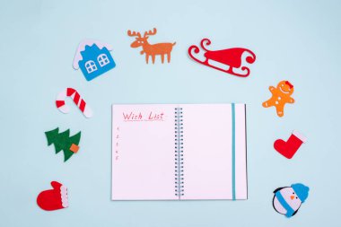Düz kompozisyon ve boş açık not defteri ile Dilek listesi ve mavi arka planda Noel oyuncakları