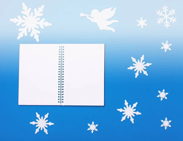 Kerst en nieuwjaar platte compositie met witte blanco notitieblok, witte engel spelen trompet en sneeuwvlokken — Stockfoto