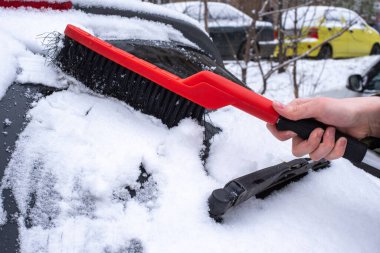 Araba sürücülerinin kış sorunları. Soğuk, karlı bir kış gününde kırmızı bir fırçayla arabasından kar temizleyen bir kadının eli..