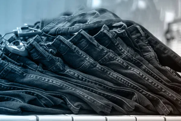 Piles of jeans on a shelf in a store, close-up, selective focus, front view, tinted blue. Shopping clothes concept.