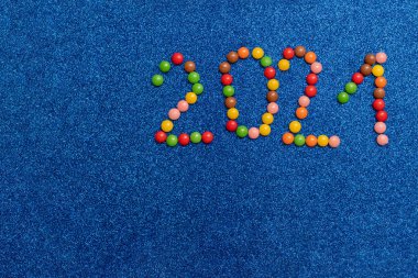 Dekorasyon konsepti, yeni yıl ve Noel için ev yapımı hediyeler. Mavi arka planda çok renkli şekerlerden yapılmış ev yapımı bir kart. Yeni yılın sembolü olarak 2021 numara