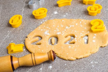 Ev yapımı kurabiye yapmaya hazırlanıyorum. Üzerine un serpiştirilmiş sarı hamurun üzerinde, 2021 sayıları yeni yılın sembolü olarak oyuluyor, yuvarlanan bir iğne ve üzerinde numaralar olan sarı formların yanında.