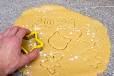 Sarı hamurun üzerinde sarı yıldız şeklindeki kadın el çeşitli yeni yıl figürleri ve 2021 numara, yakın çekim, üst manzara, kopyalama alanı. 2021 ve Noel için pişirme
