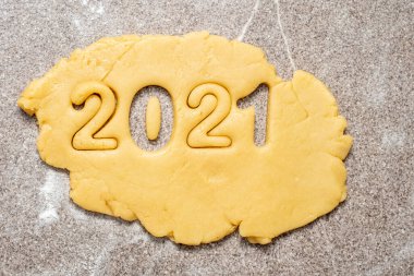 Ev yapımı kurabiye yapmaya hazırlanıyorum. Üzerine un veya pudra şekeri serpiştirilmiş sarı hamurun üzerine, 2021 sayıları yeni yılın sembolü olarak oyulmuştur, Top view, flat lay, copy space