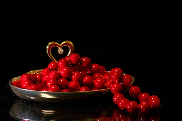 Red coral beads in a gold stand with a heart on a black background, reflection, copy space, front view, close-up, selective focus. Can be used as a postcard for women
