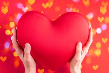 İki el, büyük kırmızı bir kalp şeklinde yastık tutar. Aşkın, ilişkilerin, dostluğun sembolü. Parlak kırmızı bir arka planda.