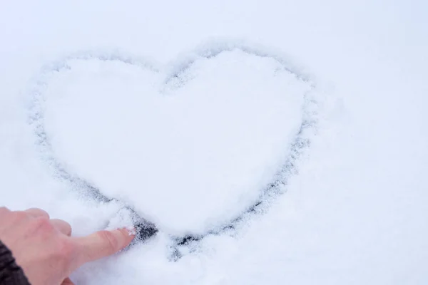 女性的手在白雪的质感上画着一个心形的爱情符号，特写，复制空间。爱的表现，以心灵的形式表现出来。情人节的概念 — 图库照片