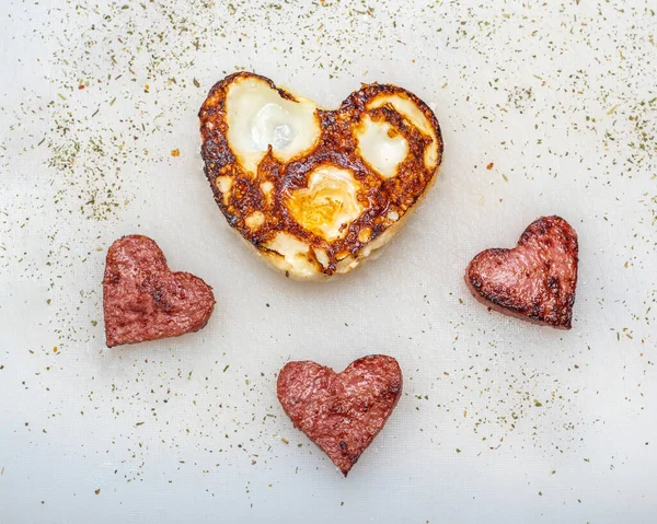Uova fritte a forma di cuore con salsicce a forma di cuore, erbe e spezie su un piatto bianco, vista dall'alto, forma quadrata. Colazione per i propri cari a San Valentino — Foto Stock