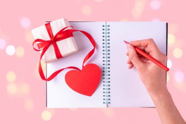 Kadın eli, beyaz, boş bir defterde kırmızı kalemle bir aşk mesajı yazar.