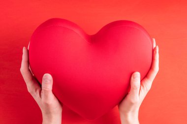 İki el, büyük kırmızı bir kalp şeklindeki yastığı tutar. Aşkın, ilişkilerin, dostluğun sembolü. Parlak kırmızı bir arka planda, yakın planda. Sevgililer Günü hediyesi.