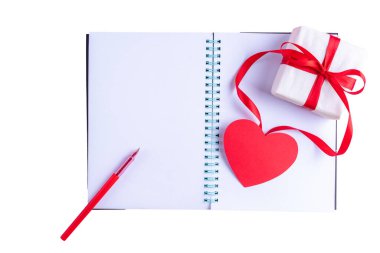 Beyaz boş defter, kırmızı kalem, kırmızı kurdeleli hediye kutusu ve beyaz üzerine izole edilmiş pembe kağıt kalp şekli.