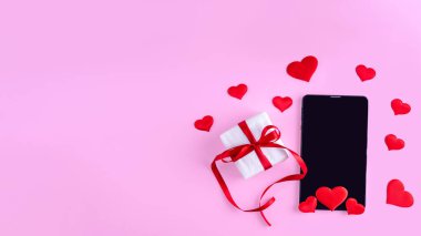 Online tebrik konsepti. Siyah boş tablet ya da pembe arkaplanda kırmızı kalpler ve hediye olan telefon ekranı