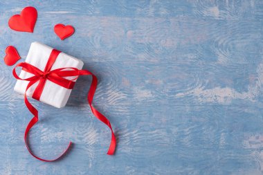 Kısa ve minimalist bir kartpostal. Beyaz kağıda sarılmış kırmızı kurdele ve kırmızı kalp şekilli hediye şık ahşap grunge mavi arka plan, kopyalama alanı