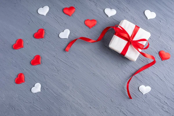 Gift in white paper with red ribbon, white and red heart shape on stylish gray grunge background, copy space — Stock Photo, Image