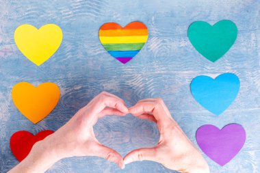 Kalp şeklinde eller ve el yapımı kağıt kalpler sıra sıra dizilmiş LGBT renkleri ve çok renkli kalpler.